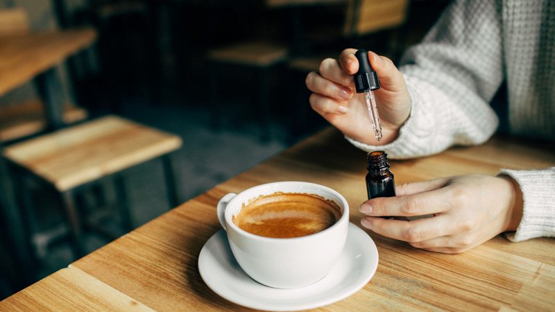 Person taking CBD oil by mixing it with his coffee