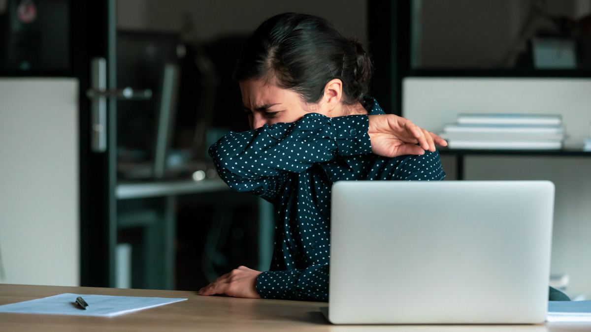 Sneezing businesswoman working on computer in office