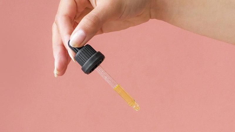 A person holding CBD Oil Drop on pink background